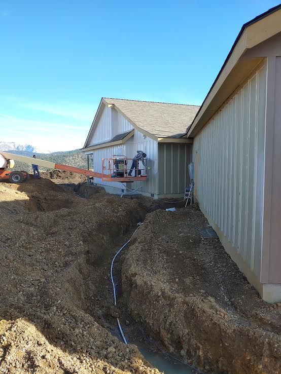 Two construction workers pouring cement into a rectangular form in front of a house.