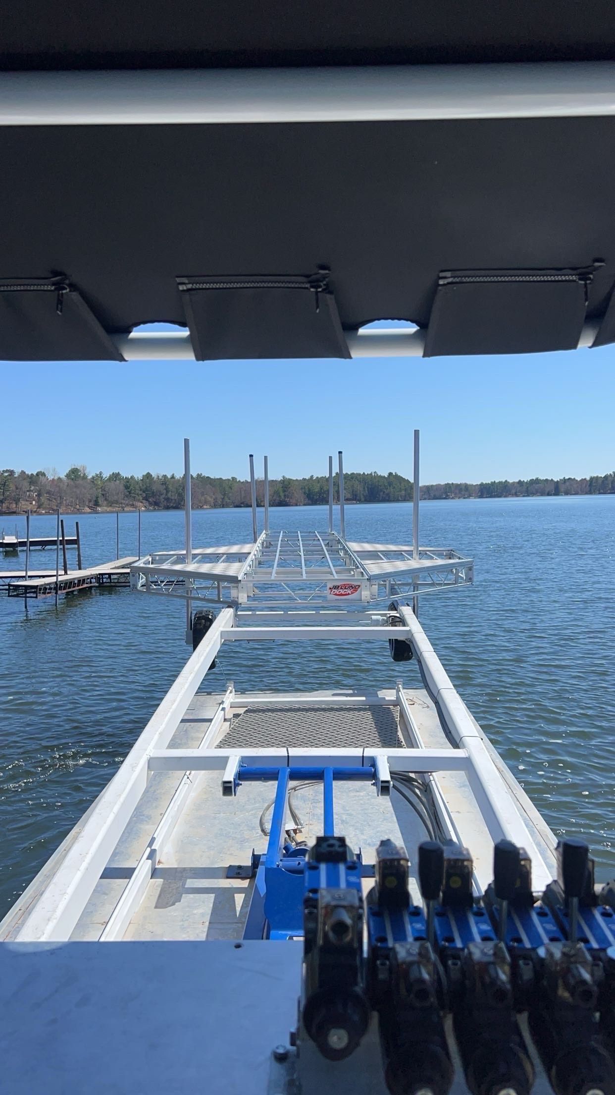 Blue boat hoist lifting a boat in a marina with boats and blue sky in the background.
