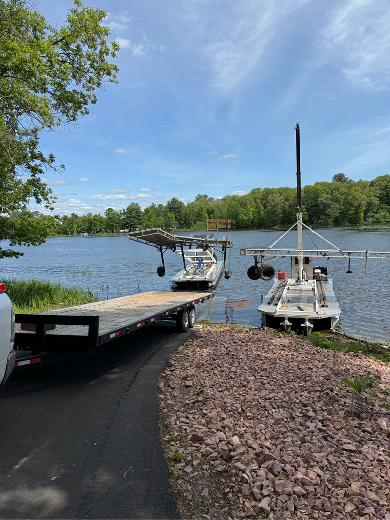 Boat docked on wooden pier at sunset. Calm water, cloudy sky, trees in the distance.