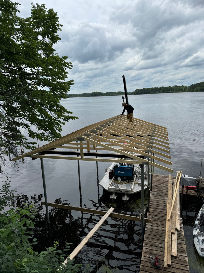 Modern white structure with stairs overlooking a green lake, surrounded by lush trees.