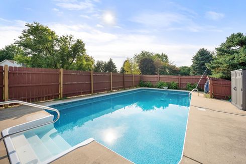 Inground swimming pool with concrete deck and safety fence surrounding the pool area.