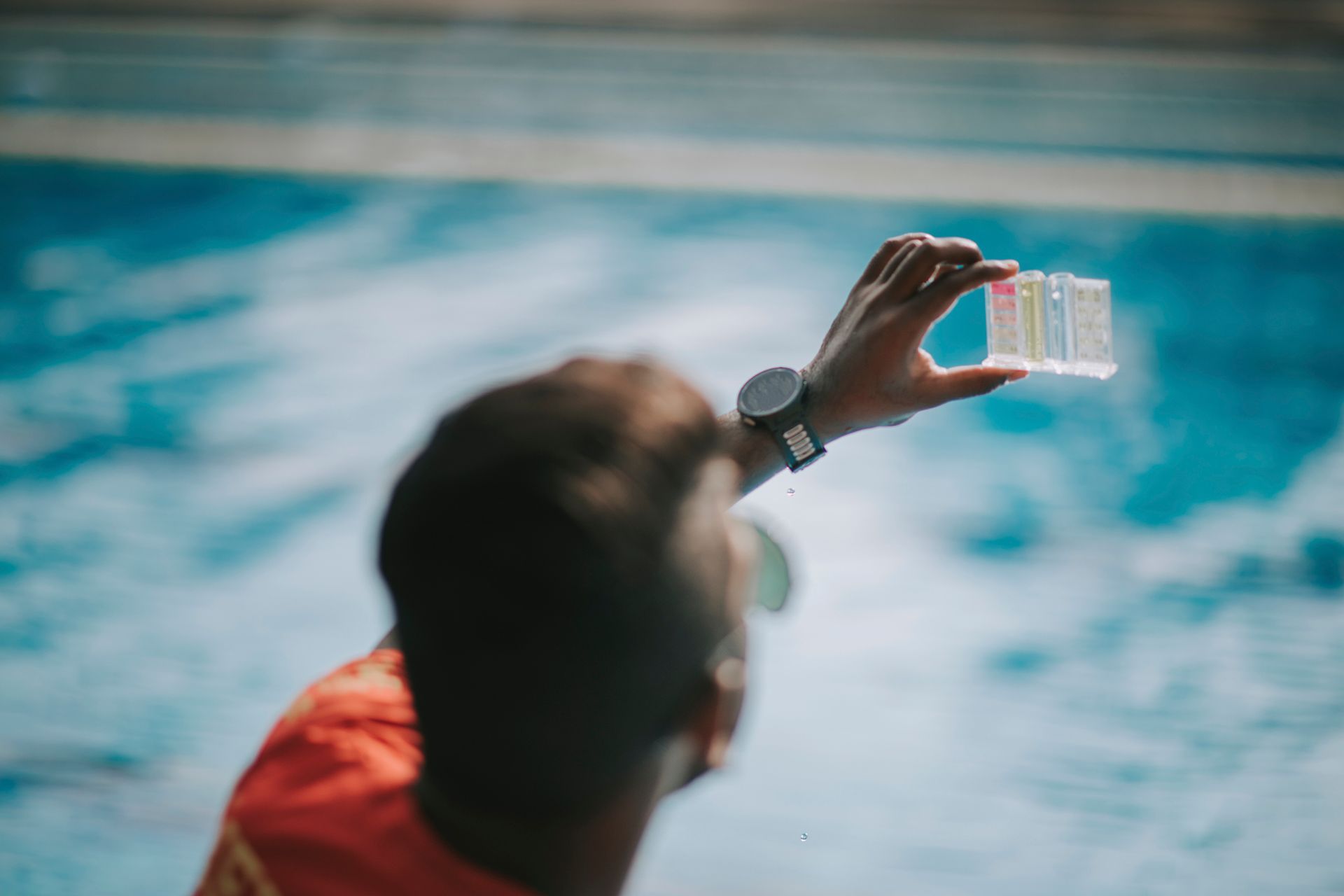 Person holding water test kit near a pool, comparing colors to check water quality.