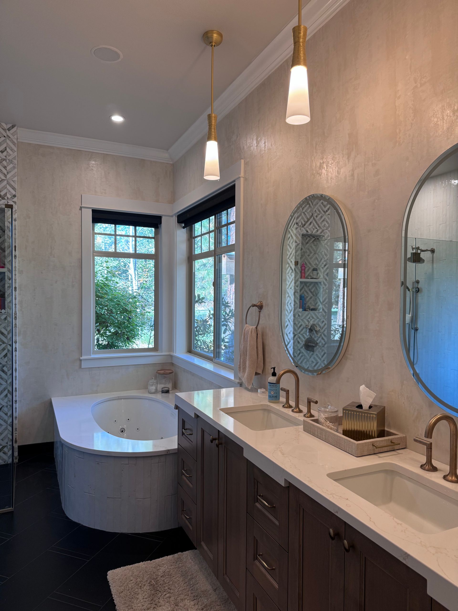 Bathroom with bathtub, double vanity, oval mirrors, and hanging lights.