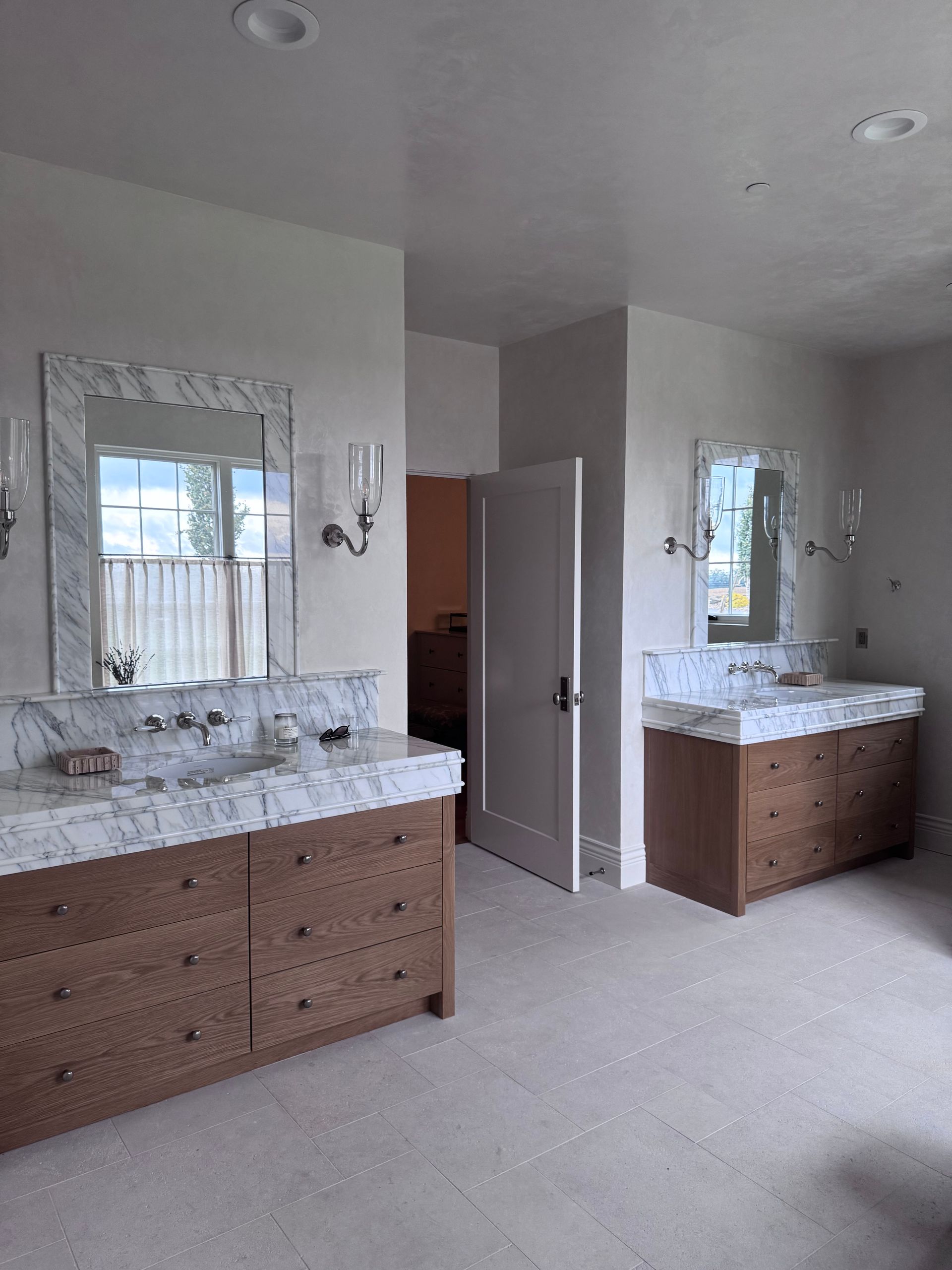 Two wood vanities with marble countertops and mirrors in a light-colored bathroom.