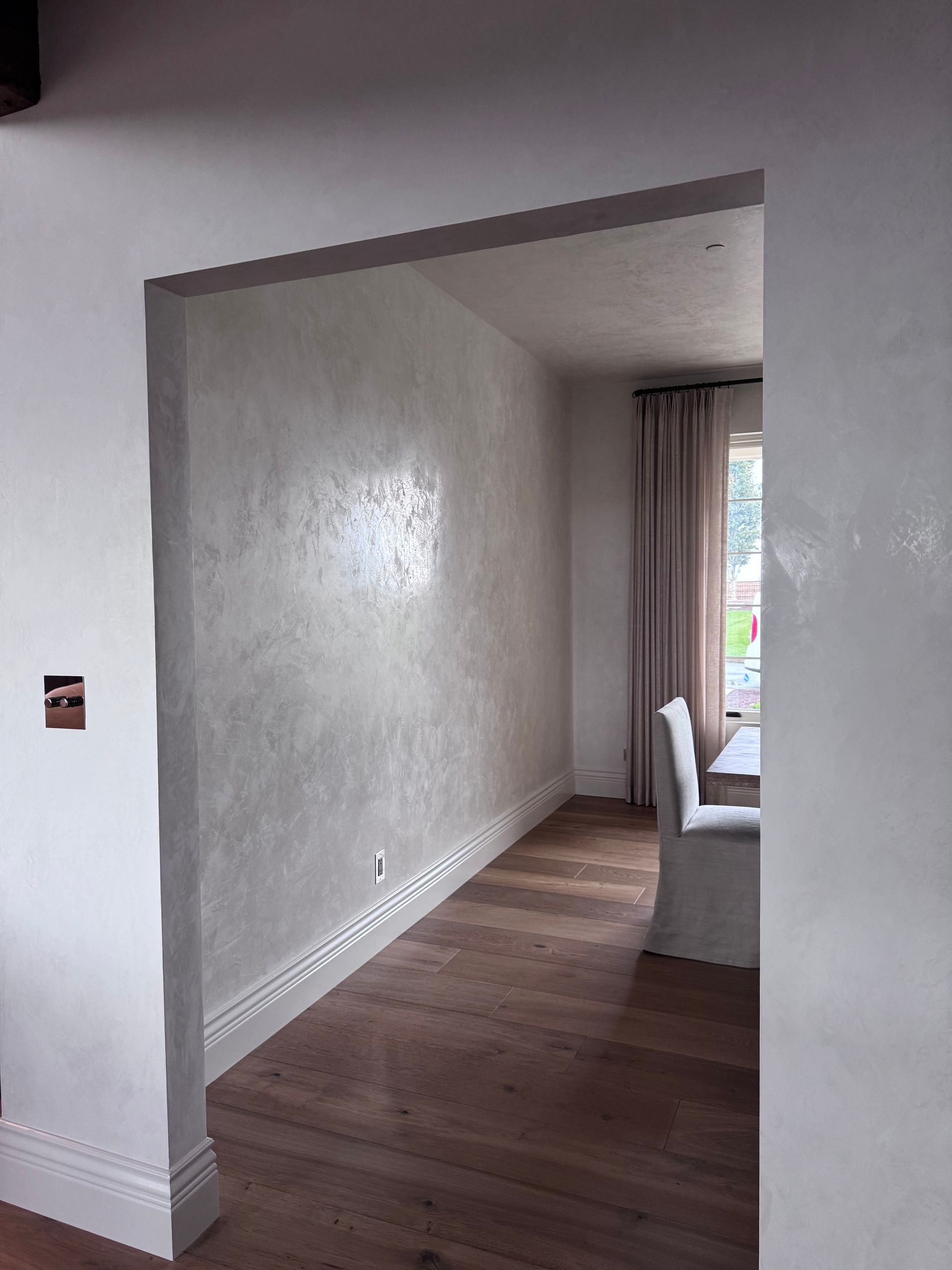 Interior doorway with a textured, silvery wall, wood floor, and a dining room visible.