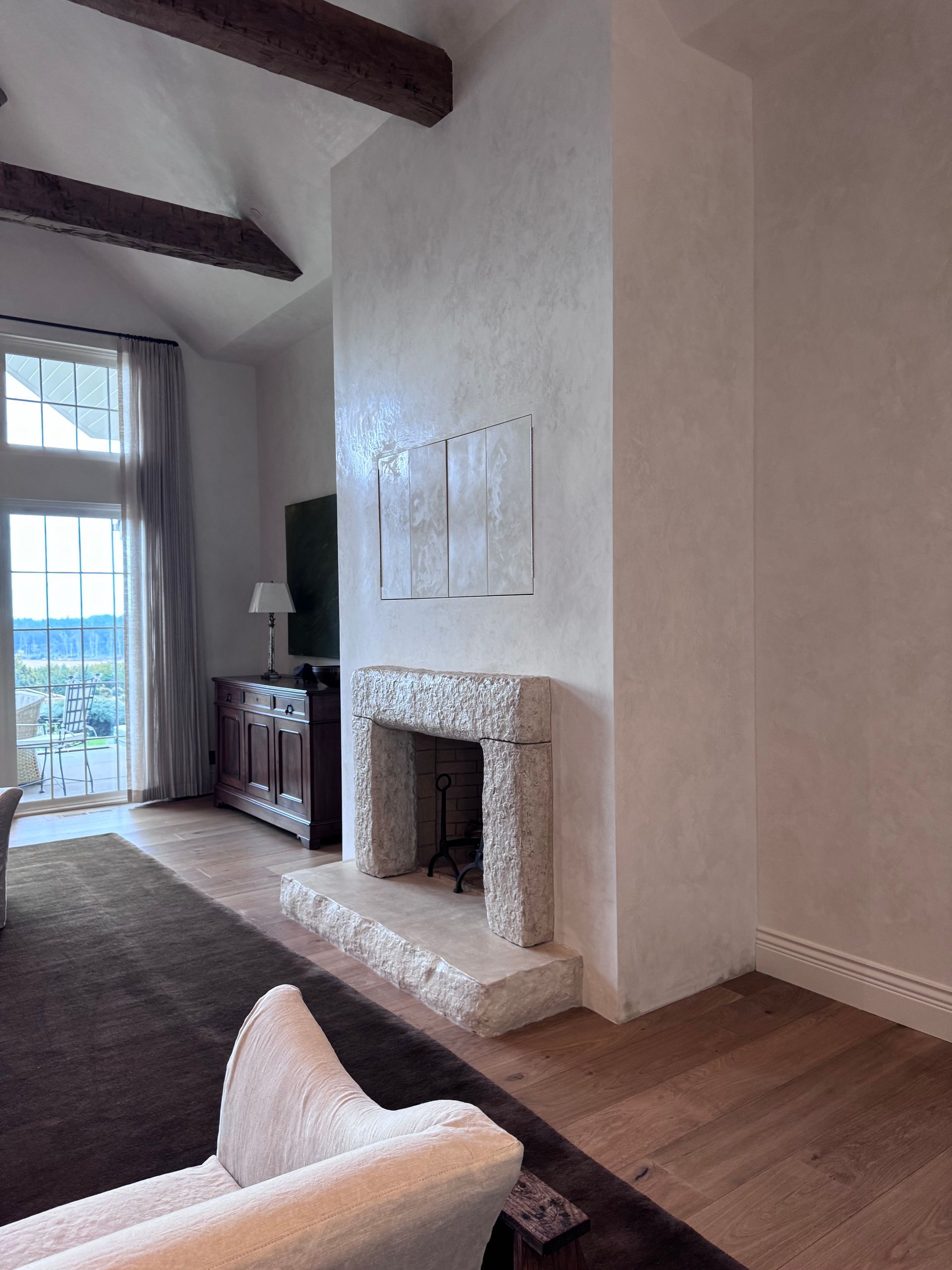 Living room with fireplace, white textured walls, and wood beams.