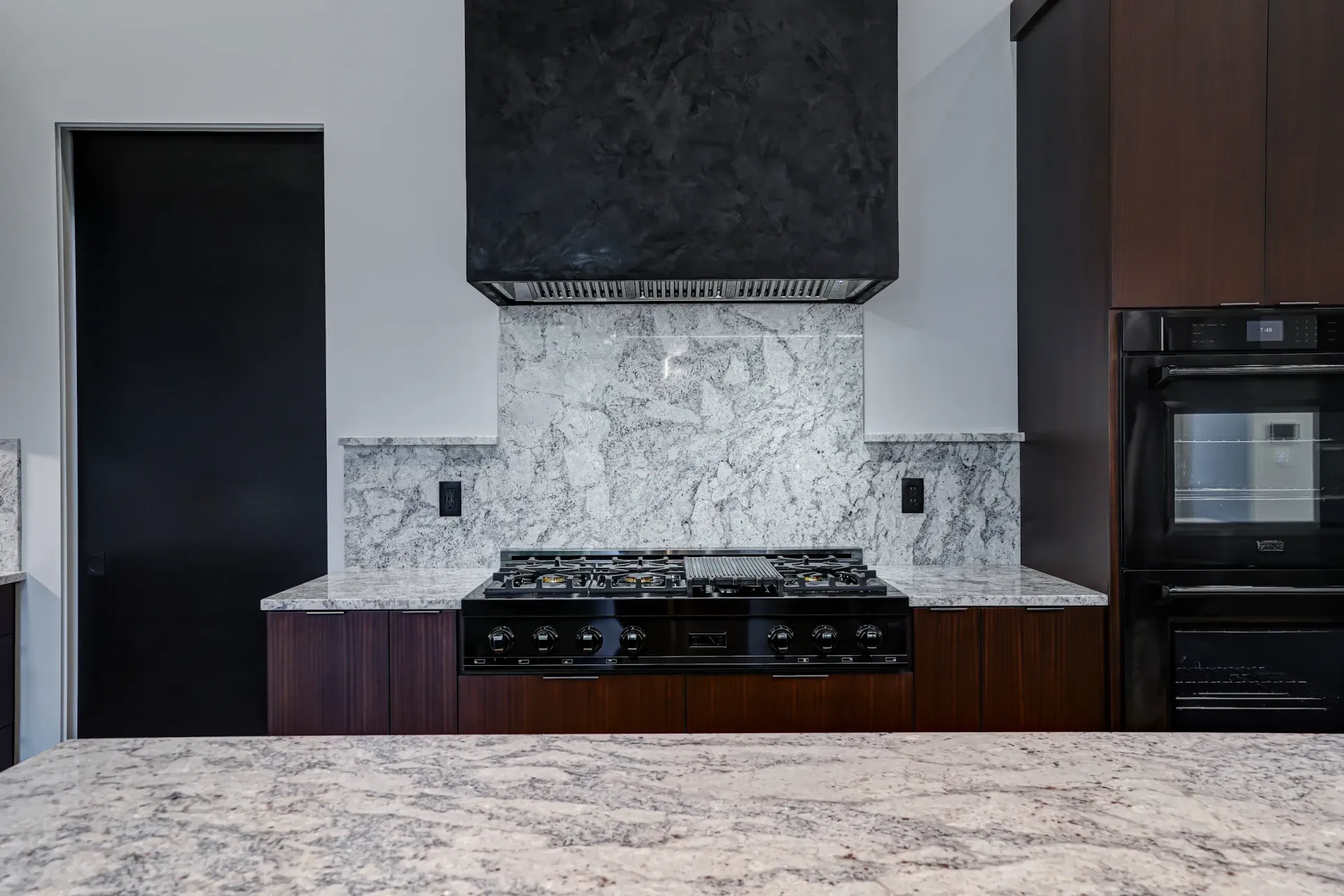 Modern kitchen with dark wood cabinets, large island, and stainless steel appliances.
