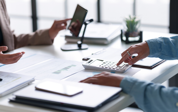 People calculating finances with documents, calculator, and tablet on a white table.