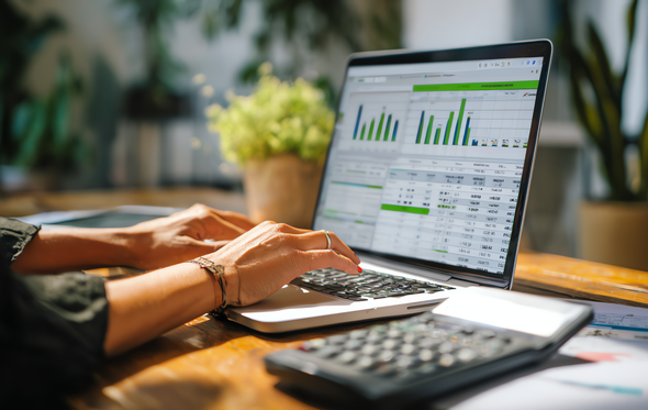 Person using a laptop, calculator nearby, displaying financial charts and data on screen.
