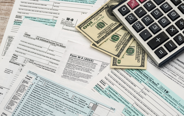 Tax forms, money, and a calculator on a desk.