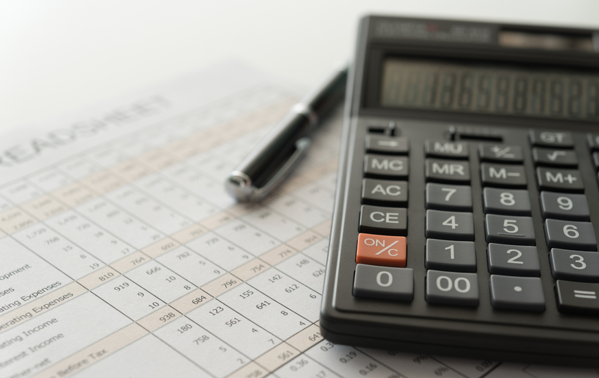 Calculator, pen, and spreadsheet on a white surface, suggesting financial calculations.