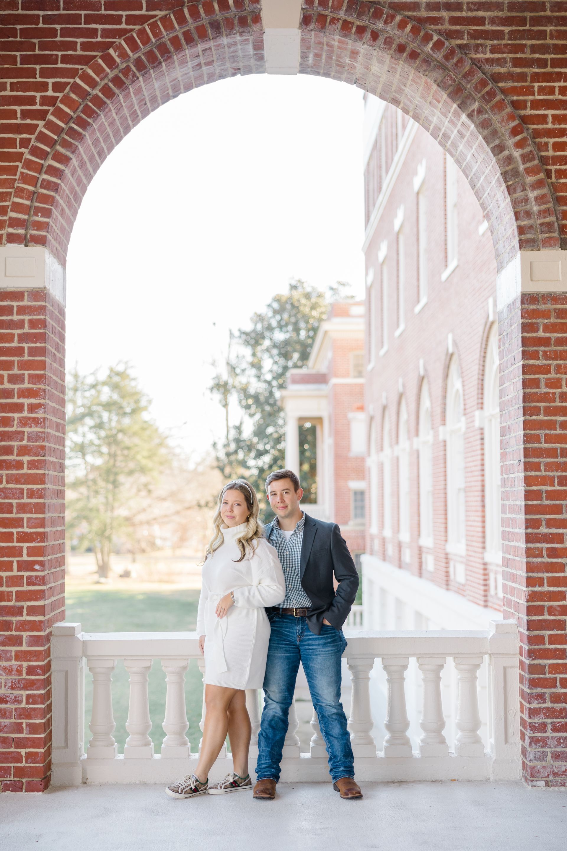A man and a woman are standing under an archway in front of a brick building.