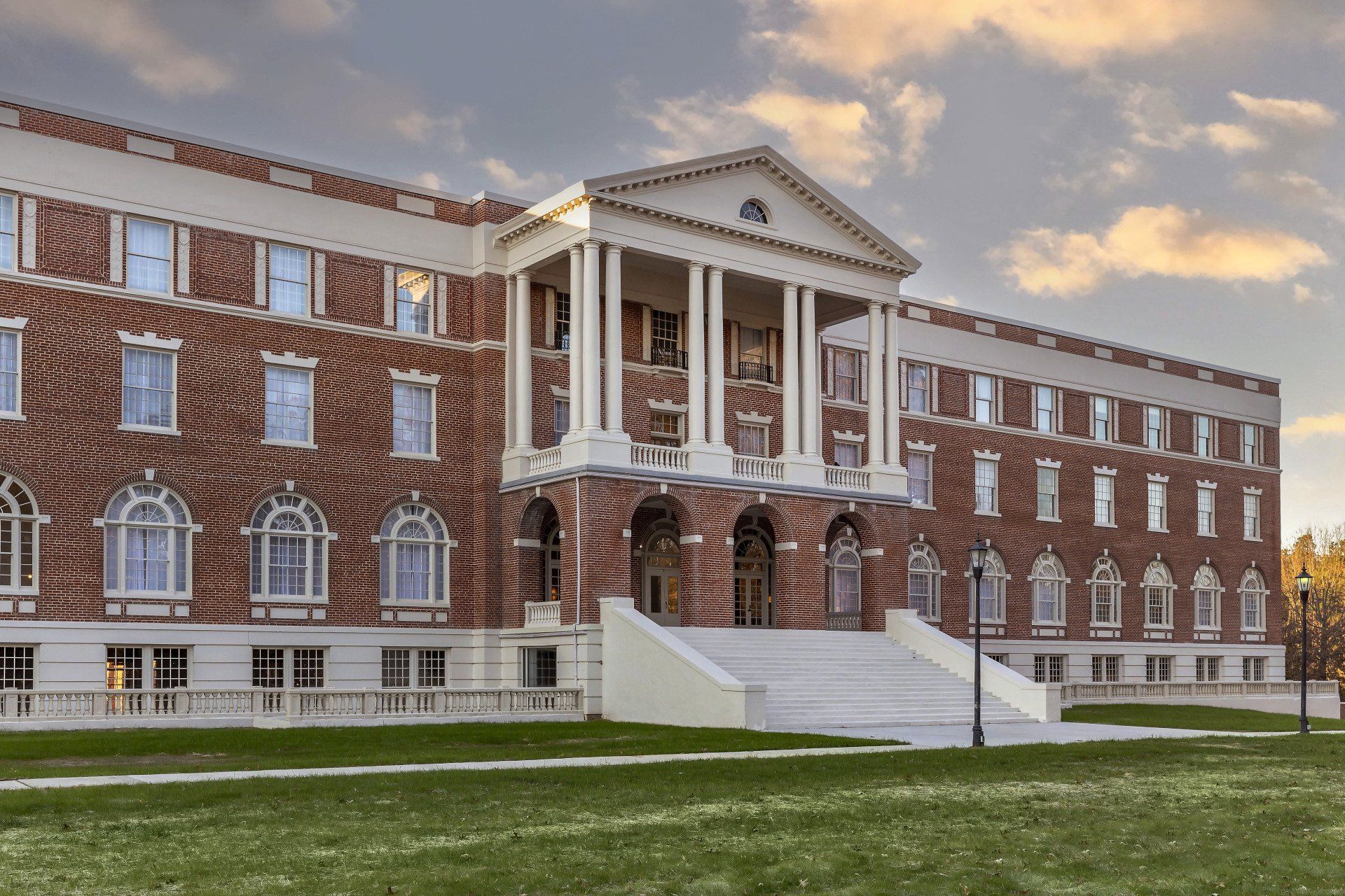 A large brick building with a porch and steps is sitting on top of a lush green field.