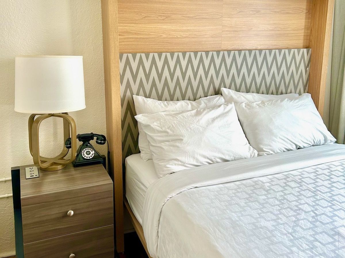 A hotel room with a bed , nightstand , lamp and telephone.