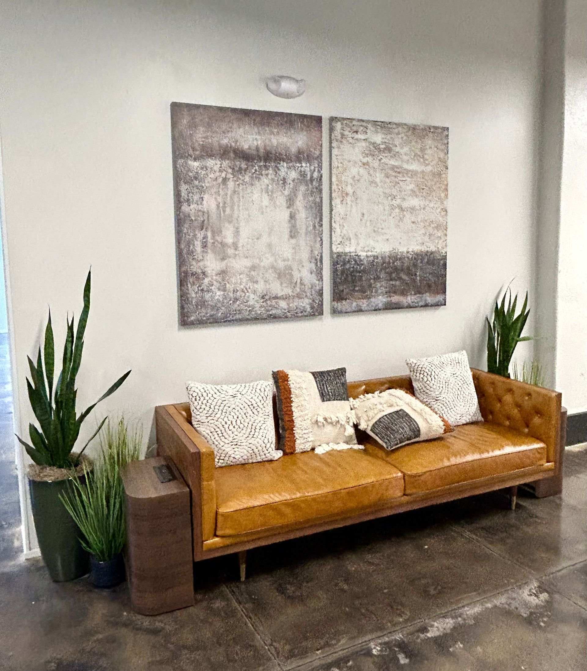 A living room with a brown leather couch and two paintings on the wall.