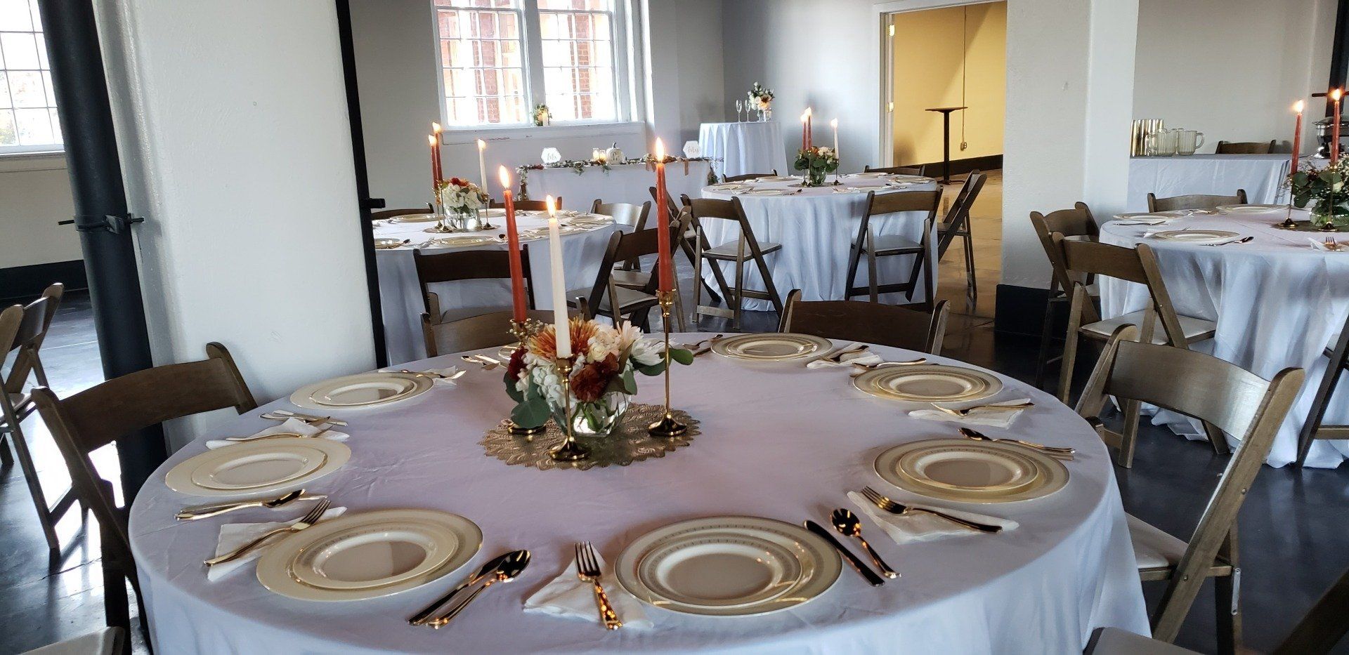 A round table with plates , silverware , and candles on it.