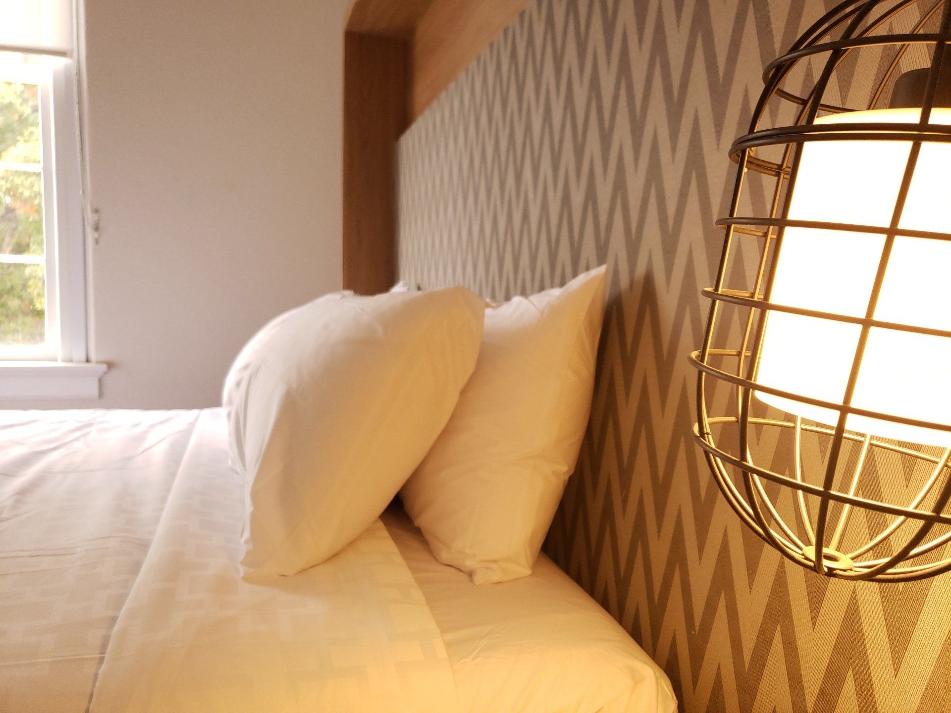A bed with white sheets and pillows in a hotel room