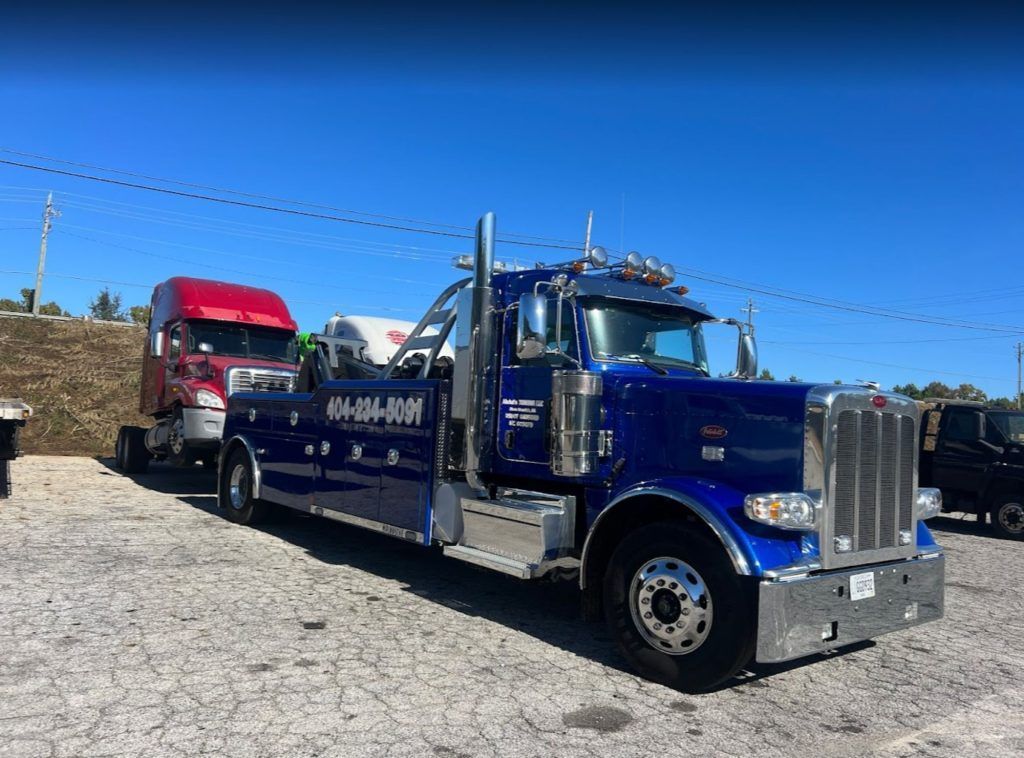 A blue tow truck is parked next to a red semi truck.