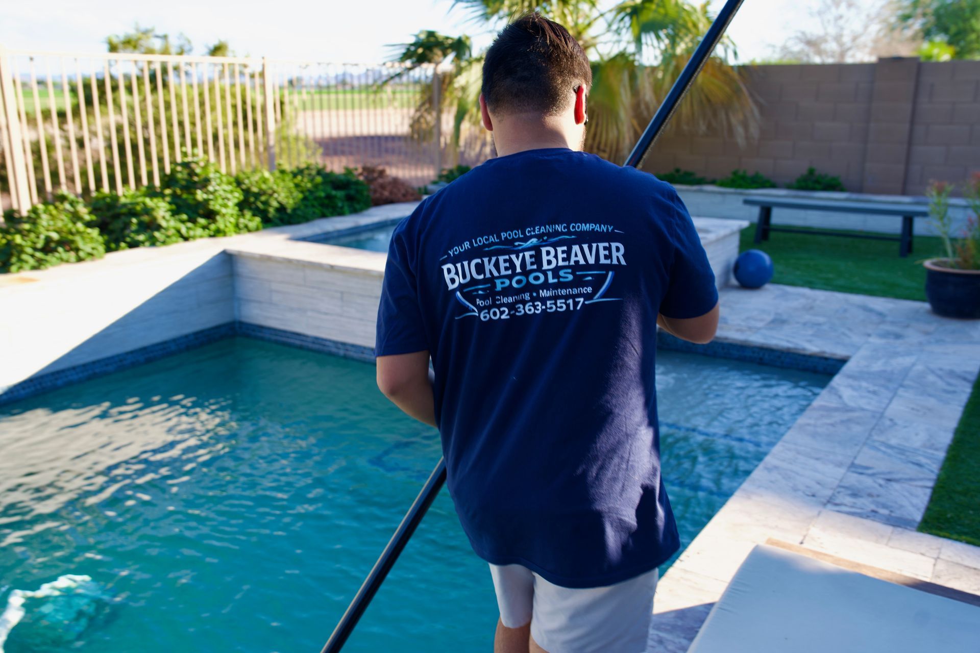 A portable pool filter pump sits on a deck, with a blue hose running into the turquoise swimming pool water.