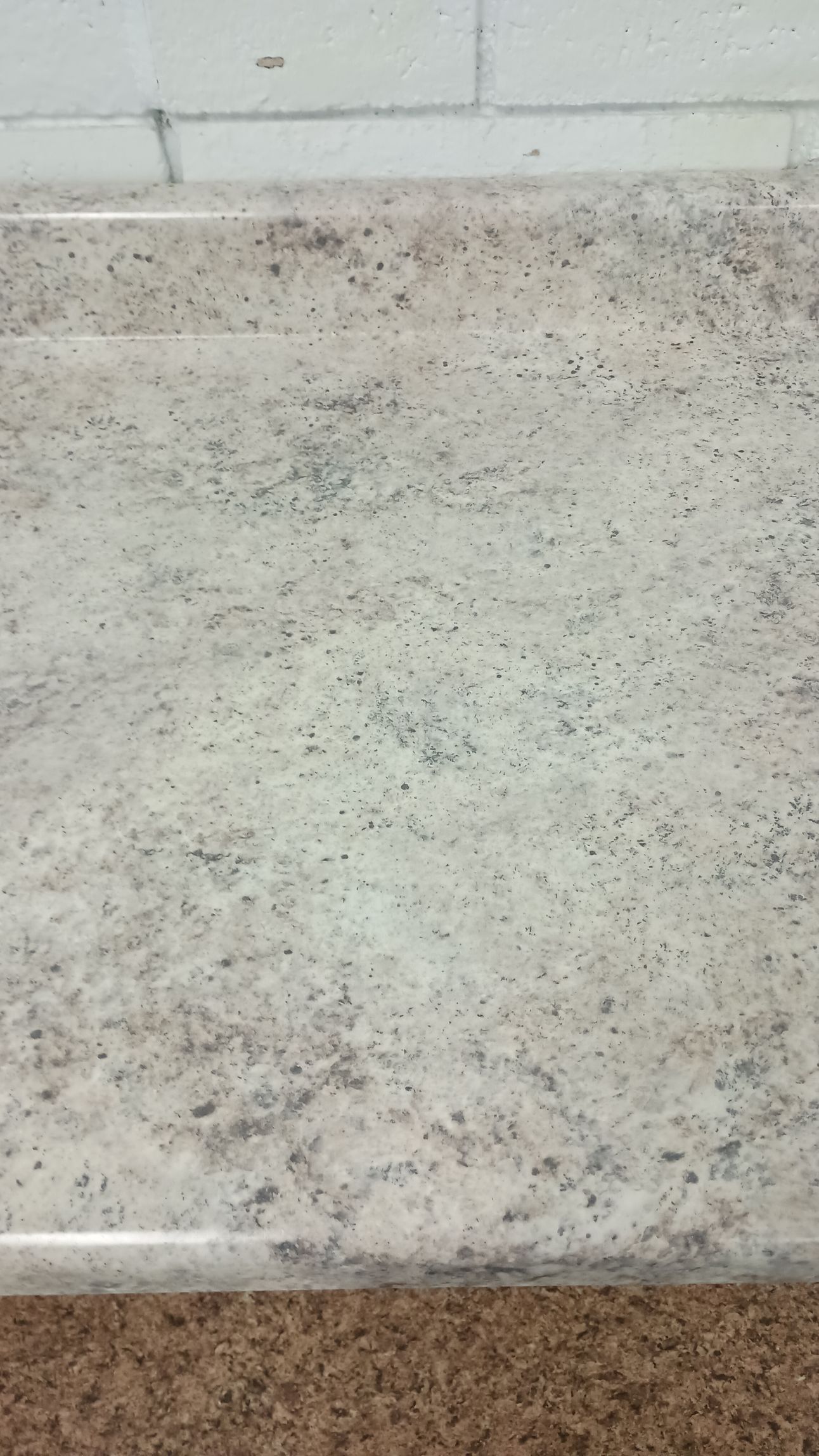 Close-up of a countertop with a speckled, light-colored surface and a light brown edge.
