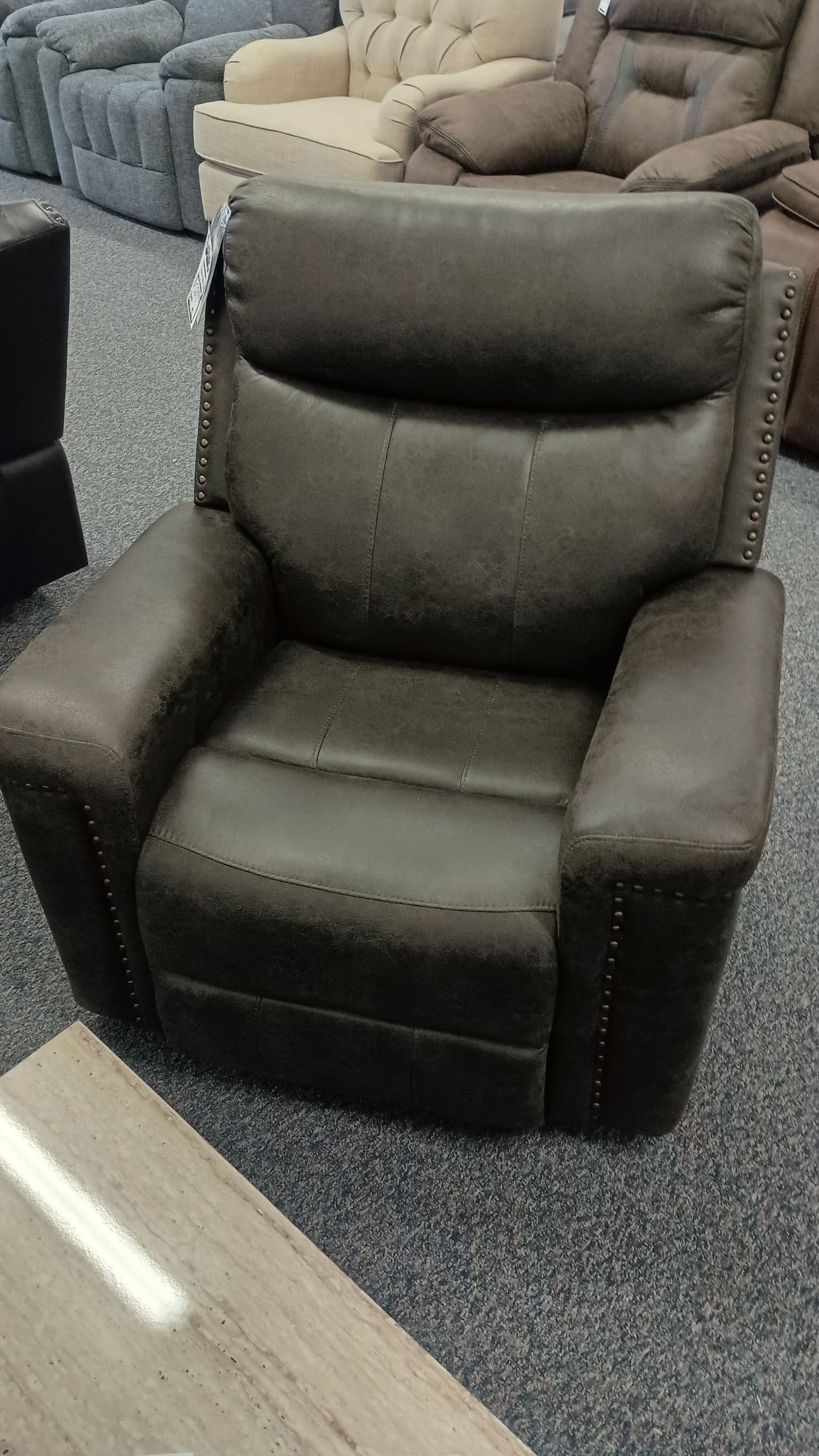 Brown leather recliner chair in a showroom, studded detail on arms.