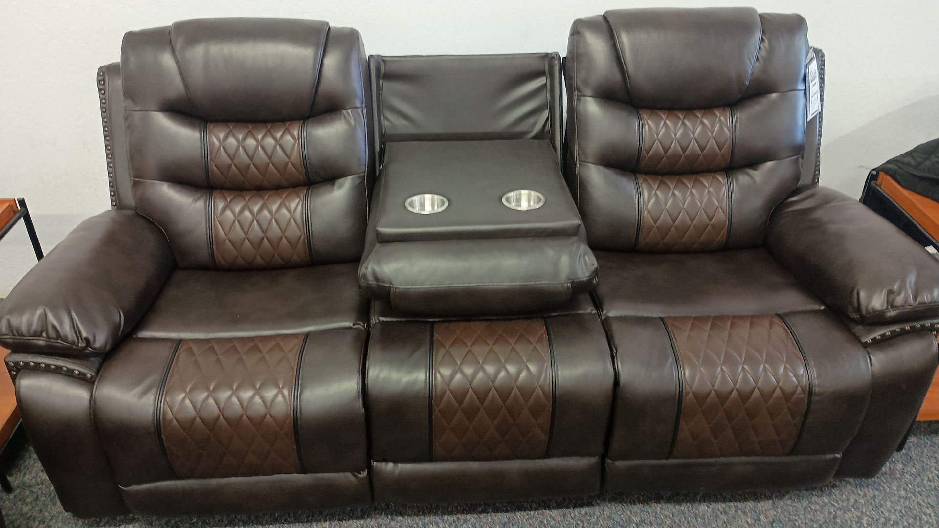 Brown leather reclining sofa with diamond patterned cushions and built-in cup holders.