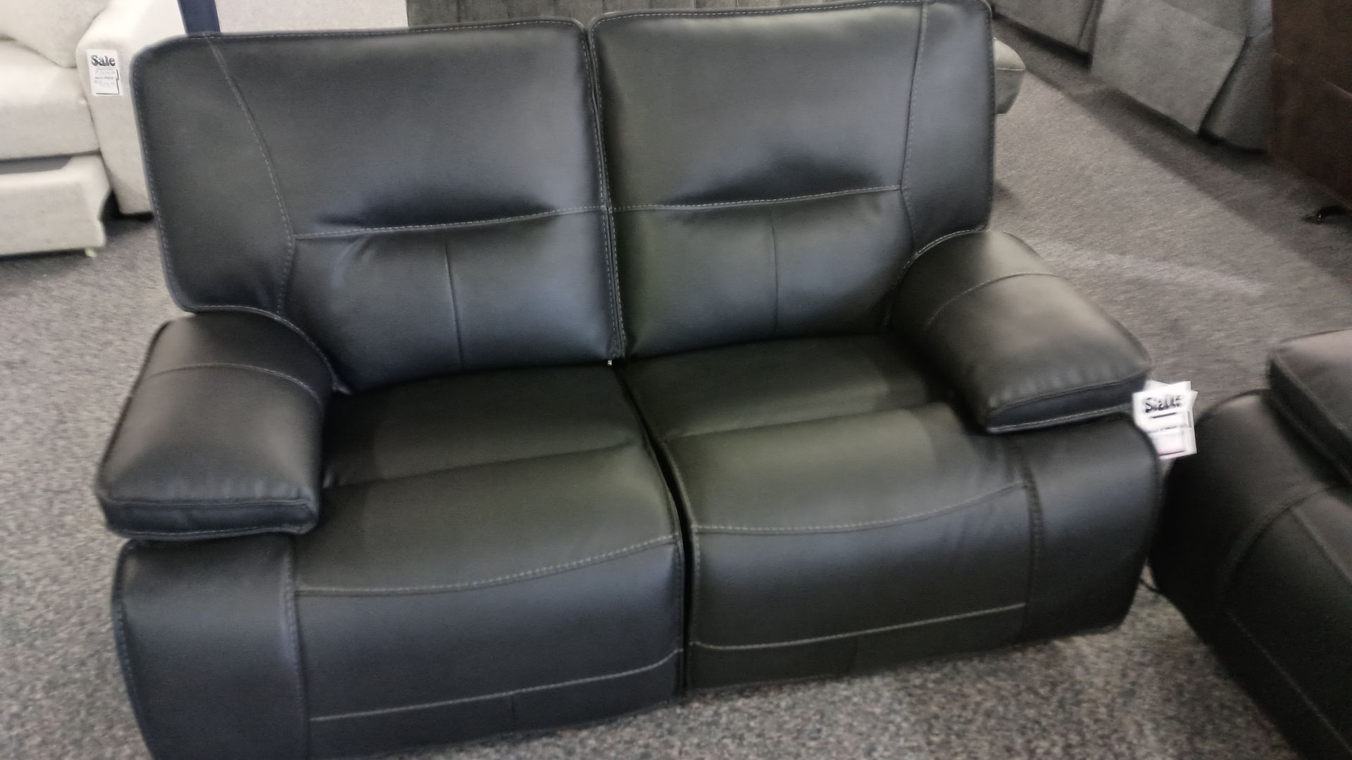 Black leather two-seater recliner sofa with thick padded arms.