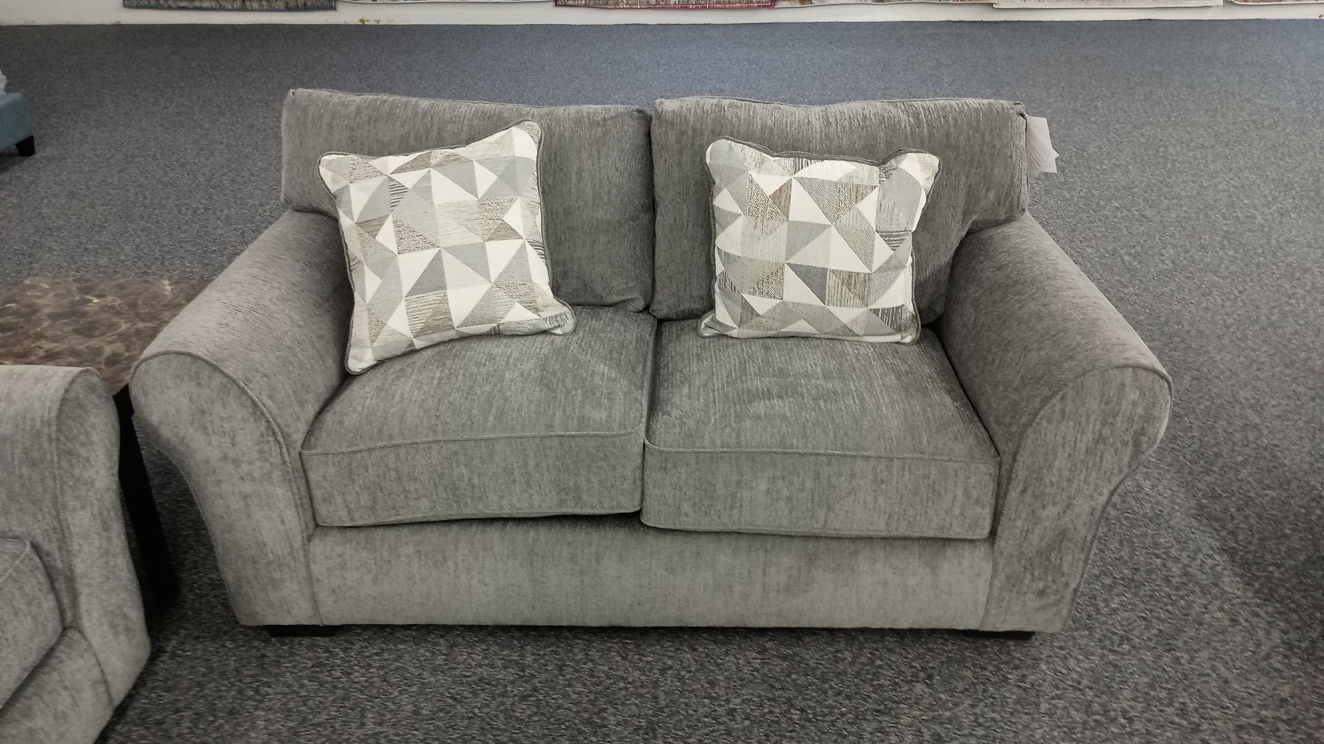 A grey couch with white pillows is sitting on a carpeted floor.