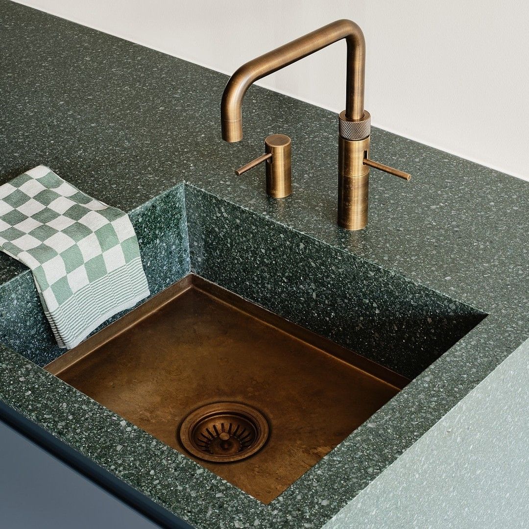 A kitchen sink with a green counter top and a brass faucet