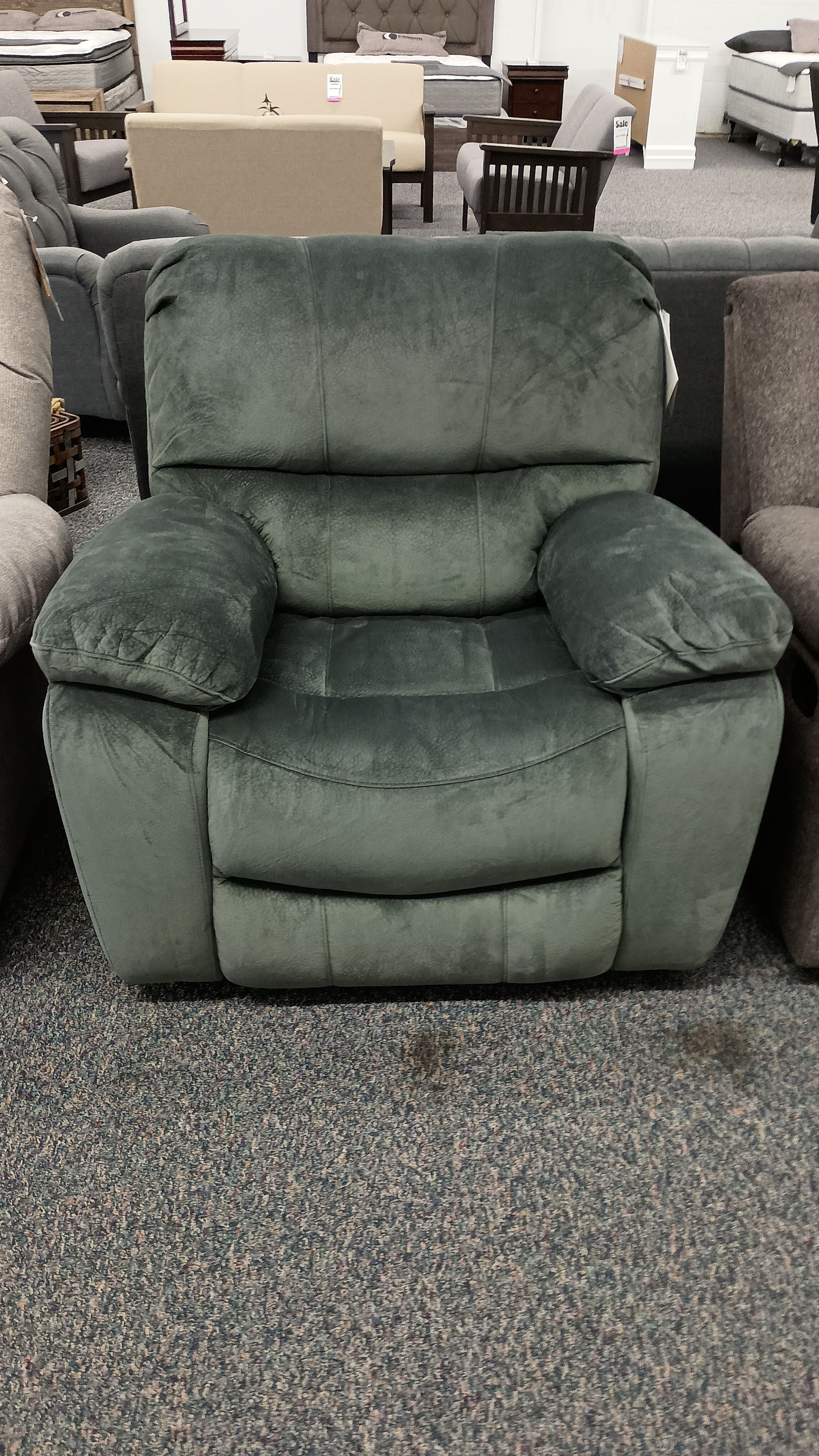 A green recliner is sitting on a carpet in a store.