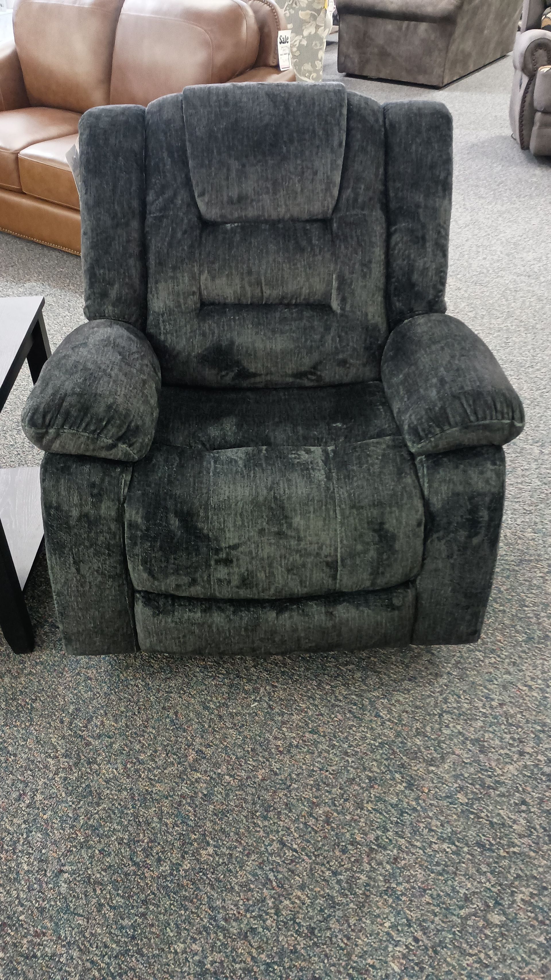 A black recliner is sitting on a carpeted floor next to a coffee table.
