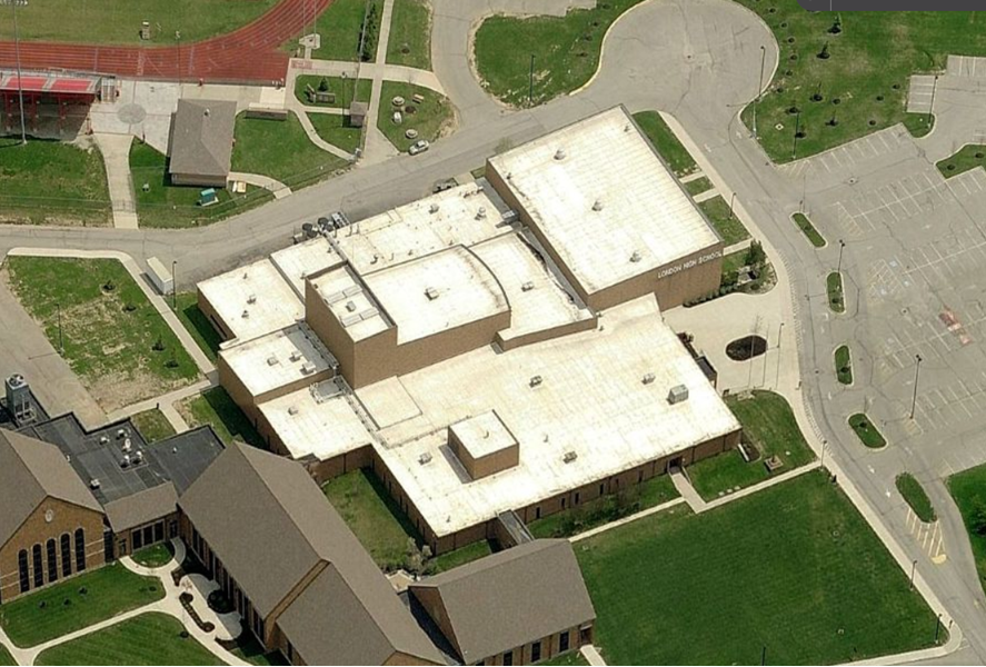 Aerial view of a school building with multiple flat roofs, next to a track and a parking lot.