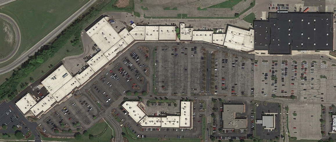 Aerial view of a large shopping mall with parking lots and surrounding green space.