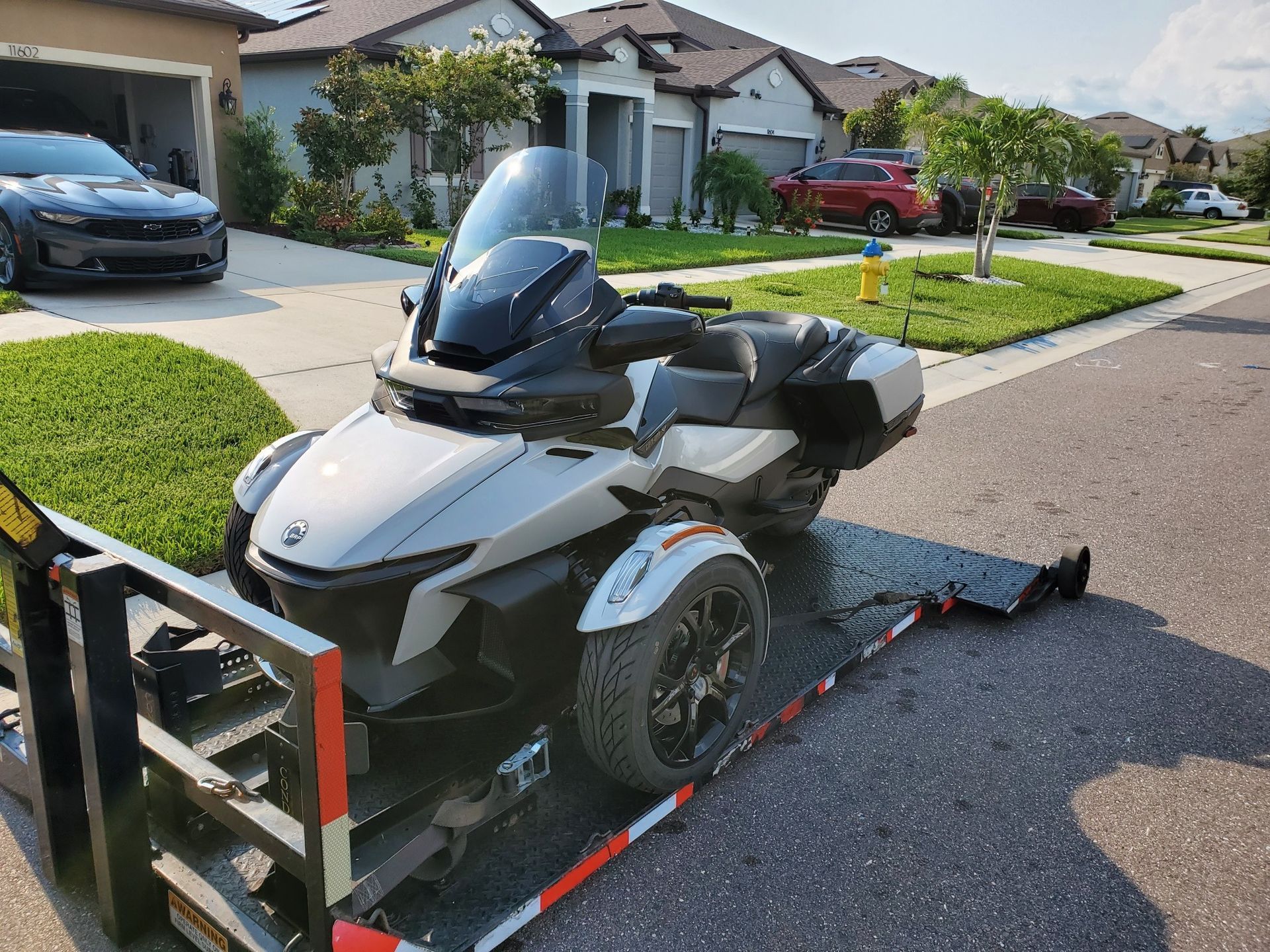 Silver Can-Am Spyder motorcycle on a trailer in a suburban neighborhood.