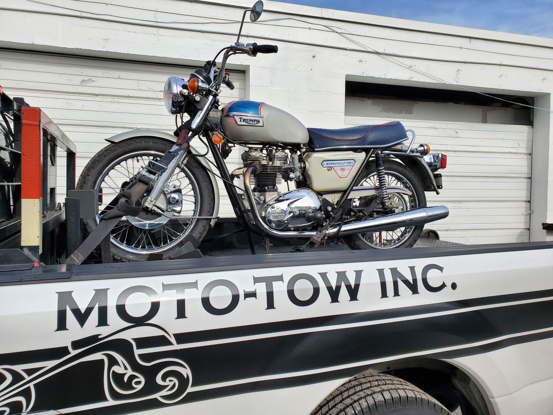 Classic motorcycle secured on a Moto-Tow truck, outside a white building.