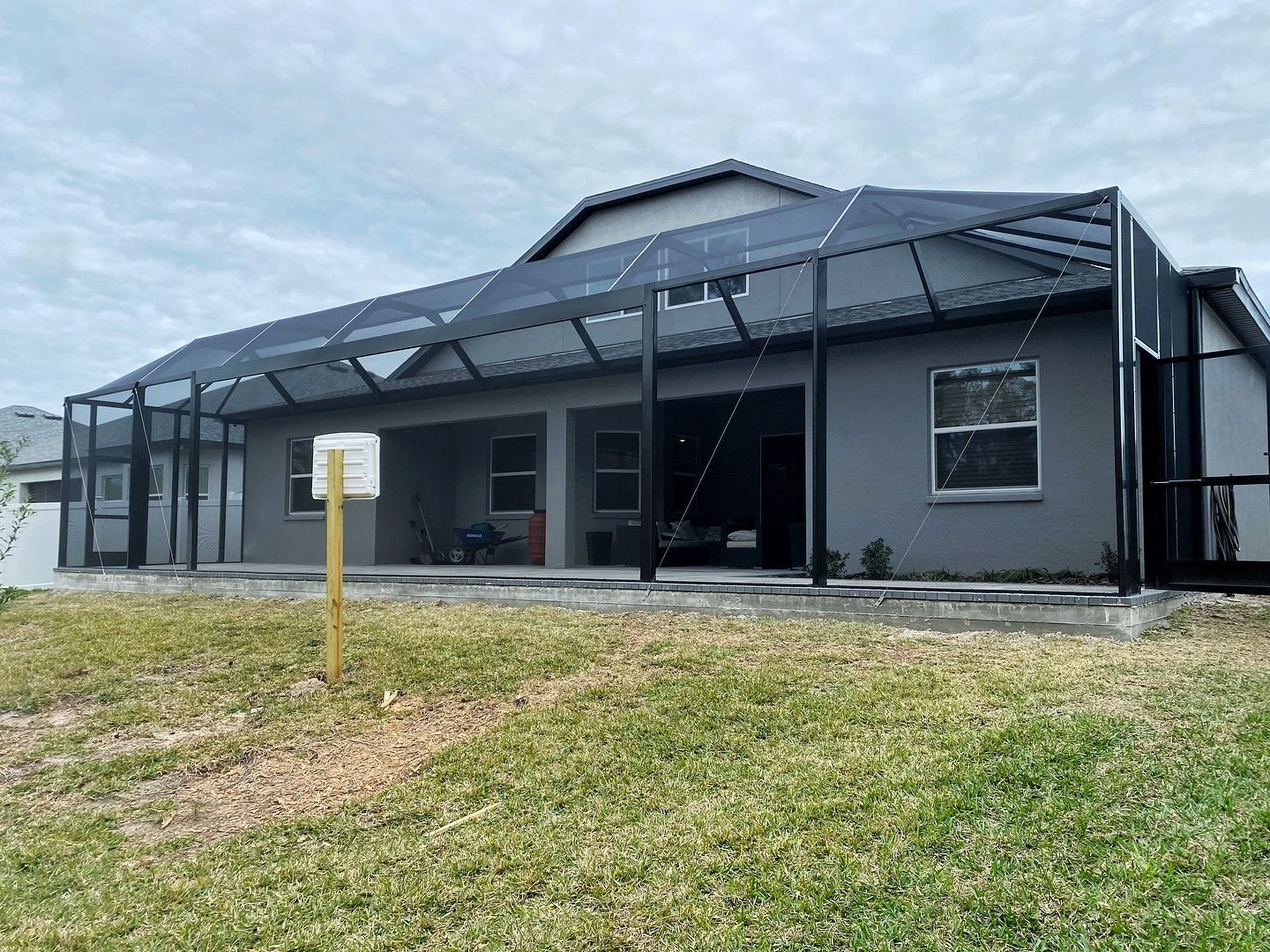 A gray house with a screened-in porch, set against a grassy yard, overcast sky.