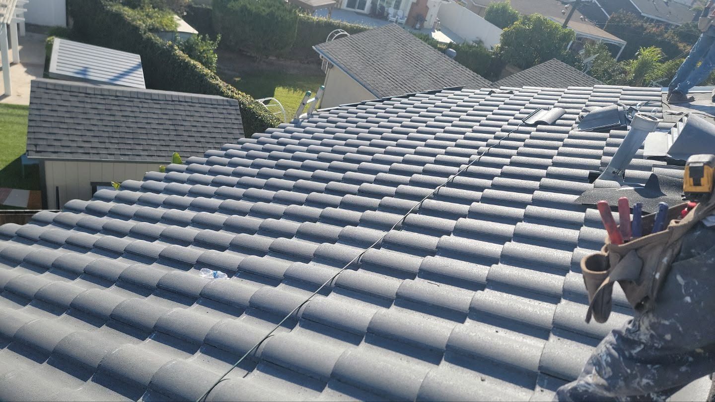 Roofers working on a gray tiled roof in a suburban neighborhood, with houses visible in the background