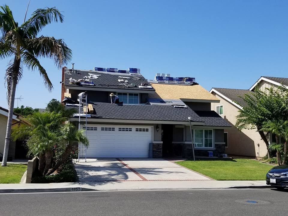 Suburban two-story house with solar panels, white garage, and palm trees under a clear blue sky
