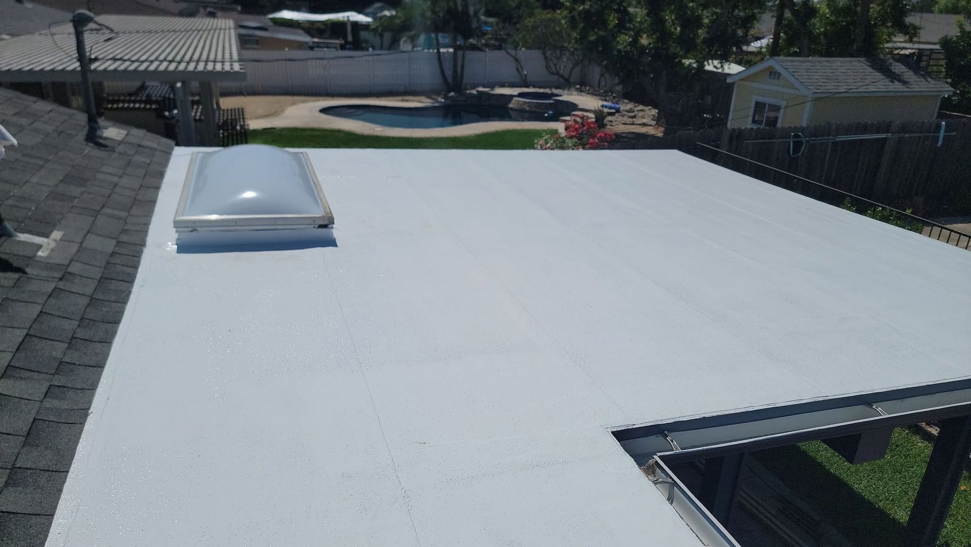 White flat roof with a skylight, viewed from above, with a pool and yard in the background