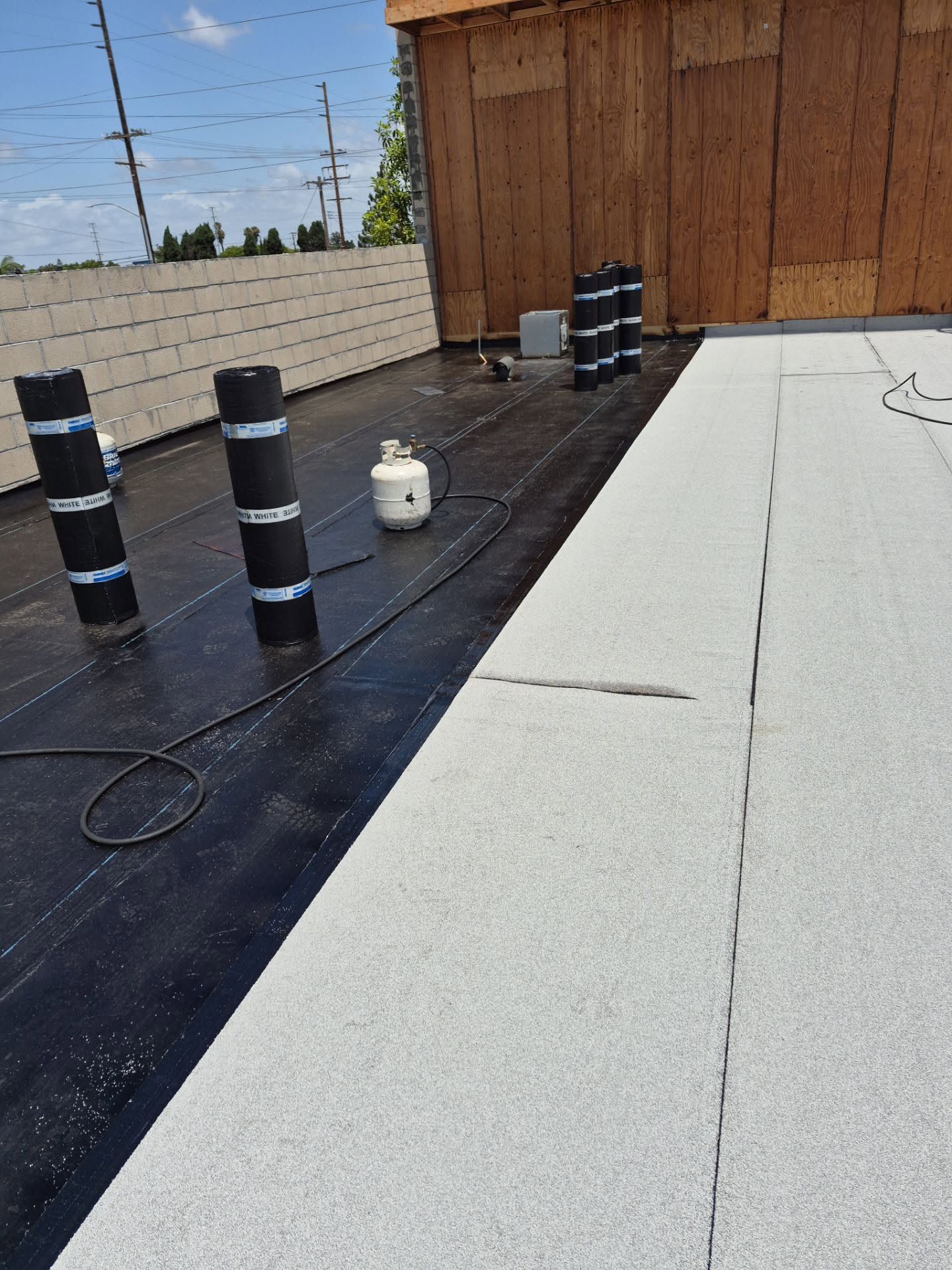 Rooftop with black vents, a propane tank, and a light-colored roof beside a wooden wall