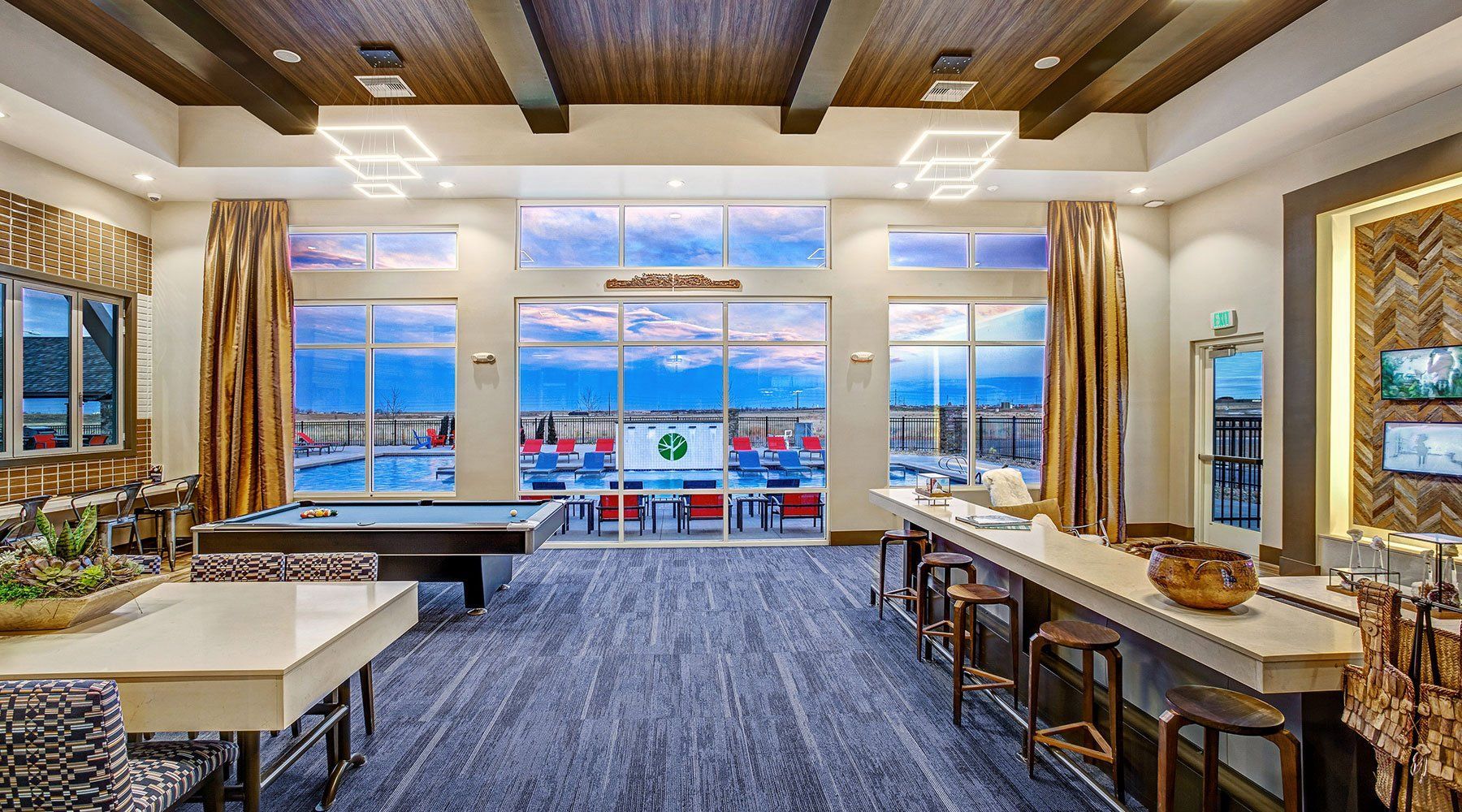 Interior of a lounge with a pool table, bar, and large windows overlooking an outdoor area.