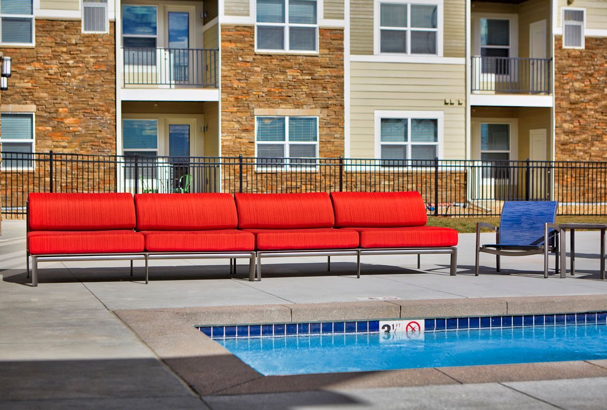 Red outdoor sofa and blue chair by a pool, with apartment building in the background.