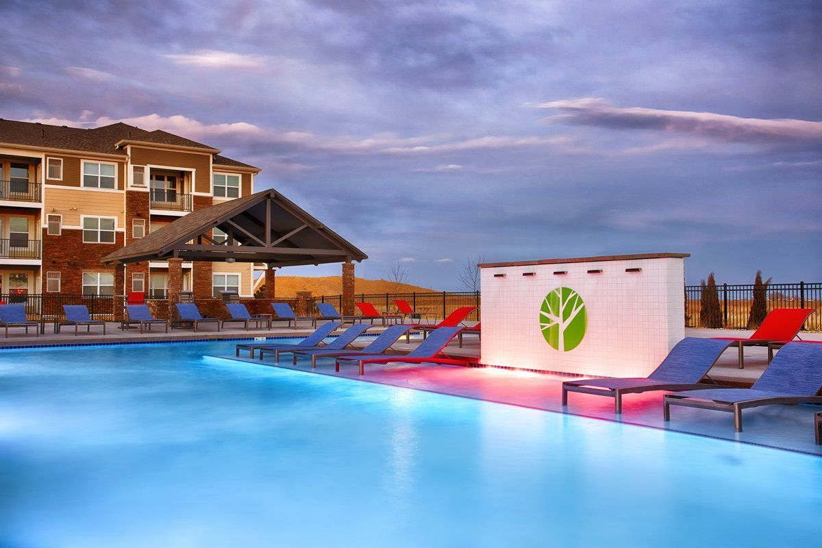 Swimming pool at dusk with lounge chairs, cabana, and apartment building.