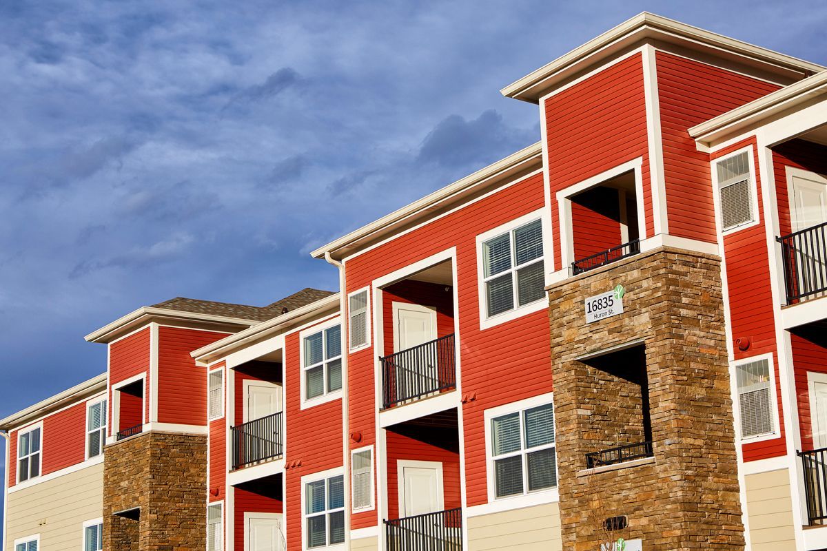 Red and beige apartment building with stone accents against a cloudy blue sky.