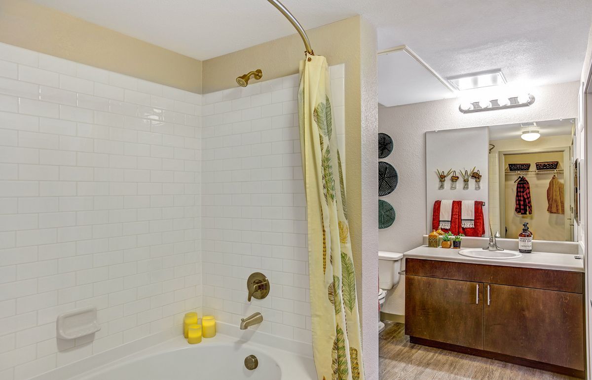 Bathroom with a white-tiled shower, tan walls, a yellow shower curtain, and a wooden vanity with a mirror.