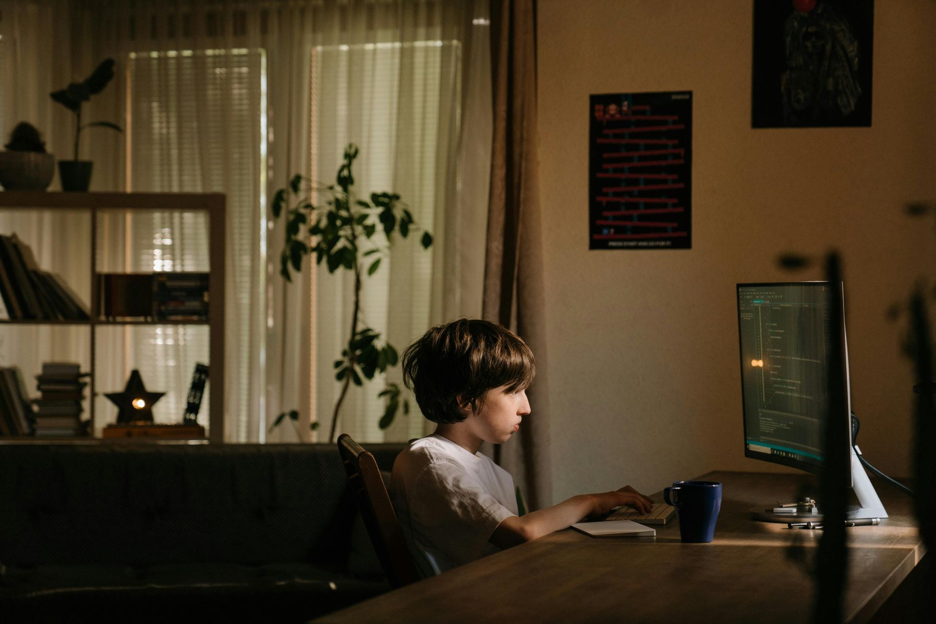 An adolescent boy on a computer in a dark room.