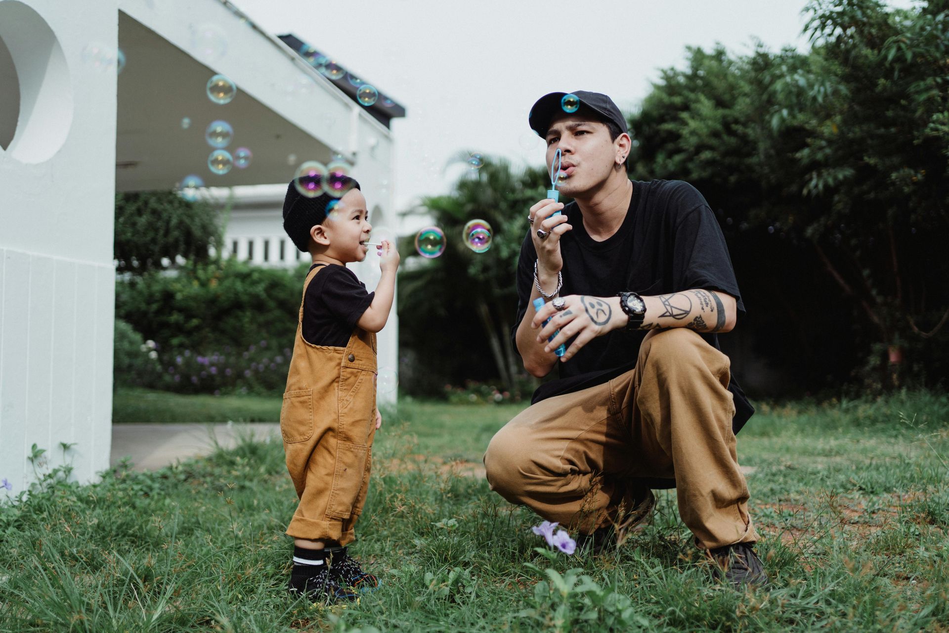 A young father and boy blowing bubbles in a yard.