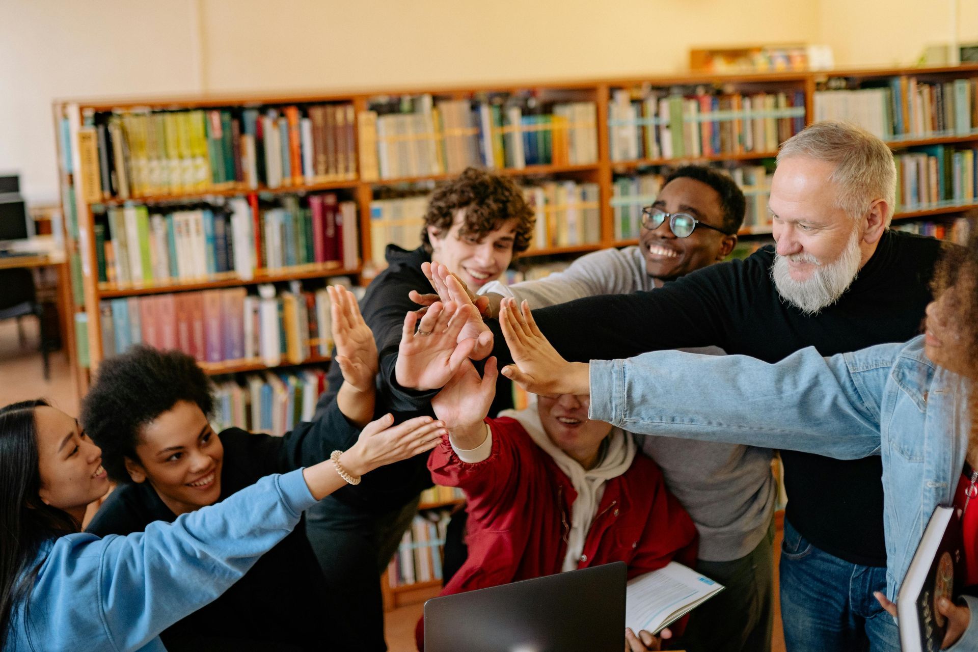 A group of youth and an older man high-fiving in a library