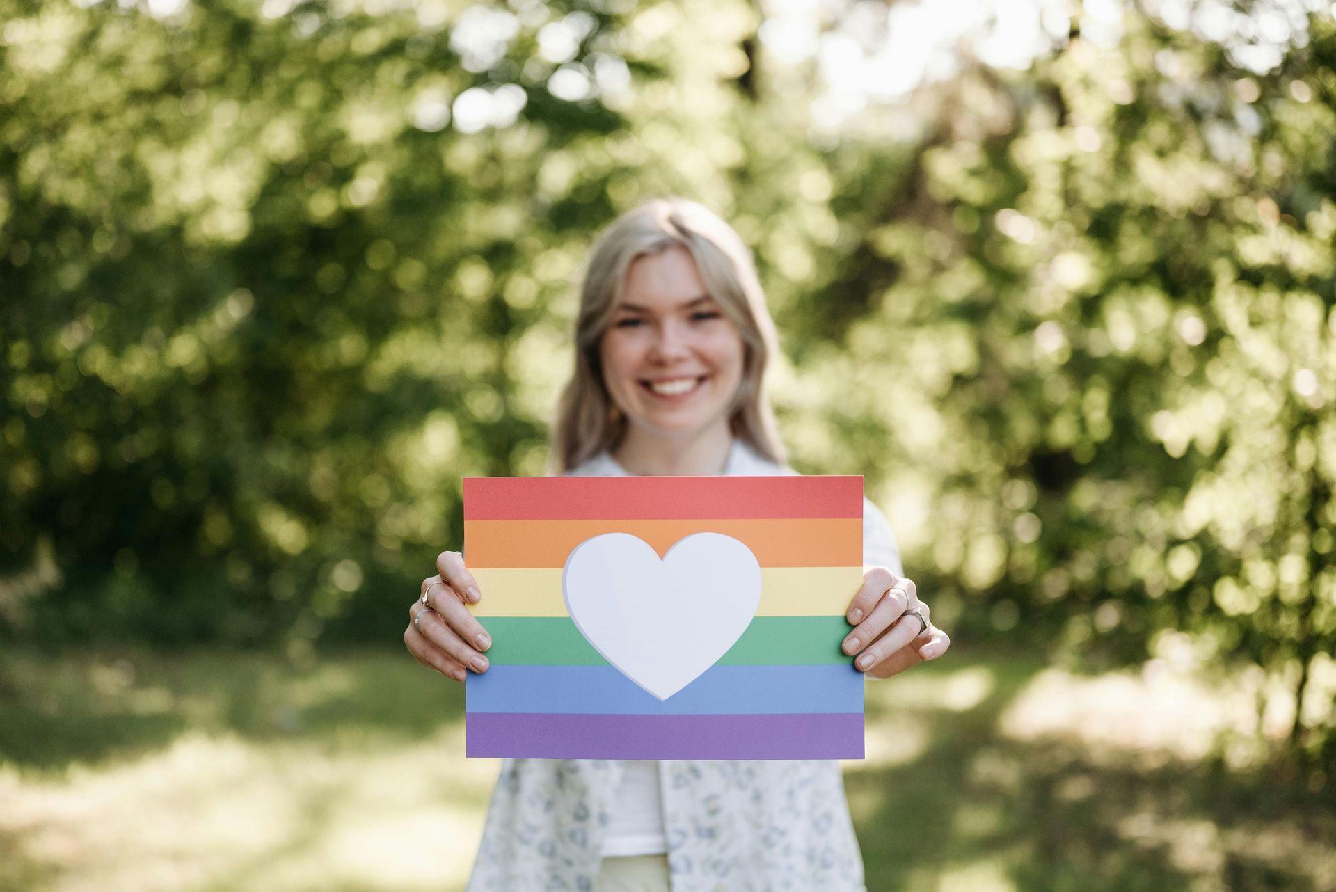 A young woman holding a pride flag with a heart on it.