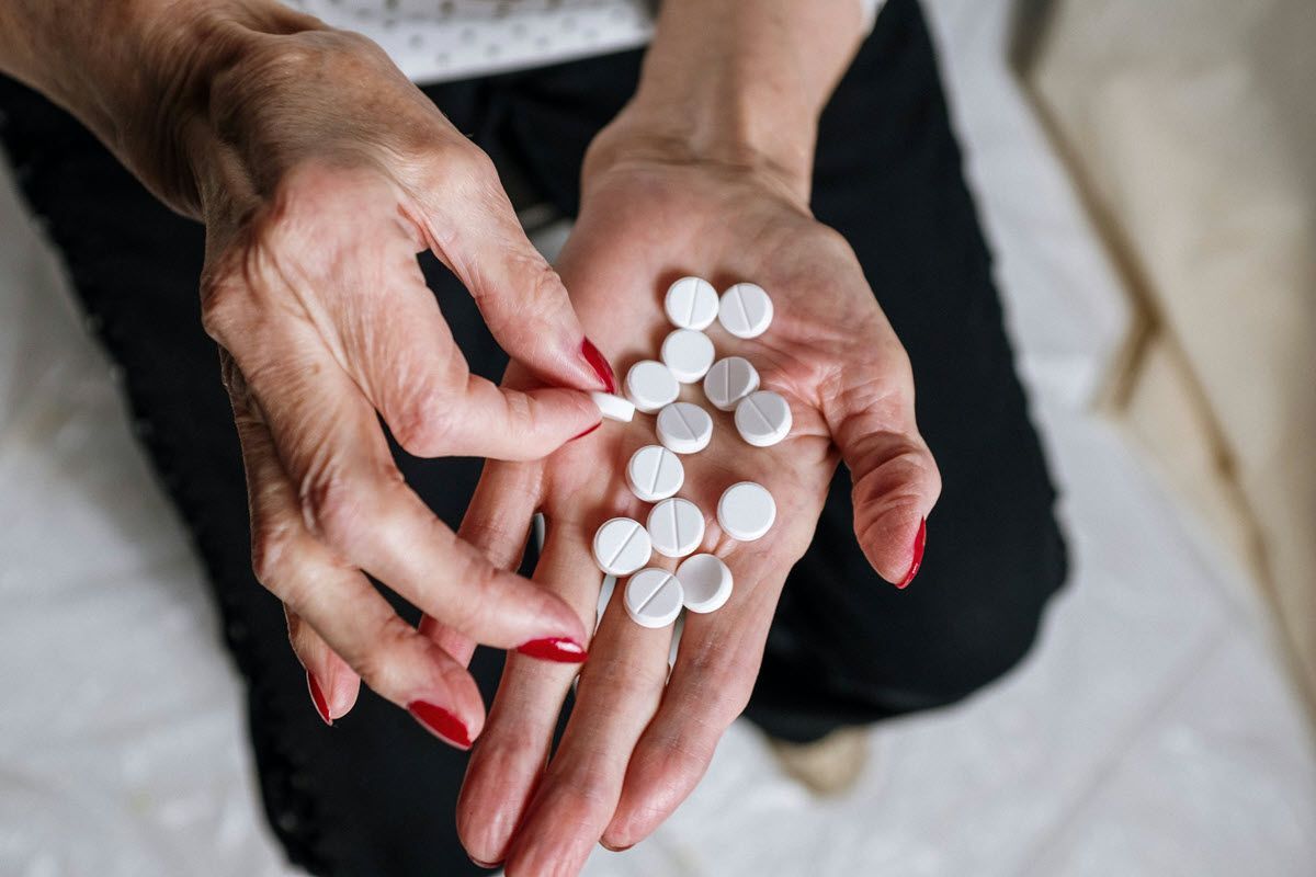 Hands with red nails holding several white pills over a lap.
